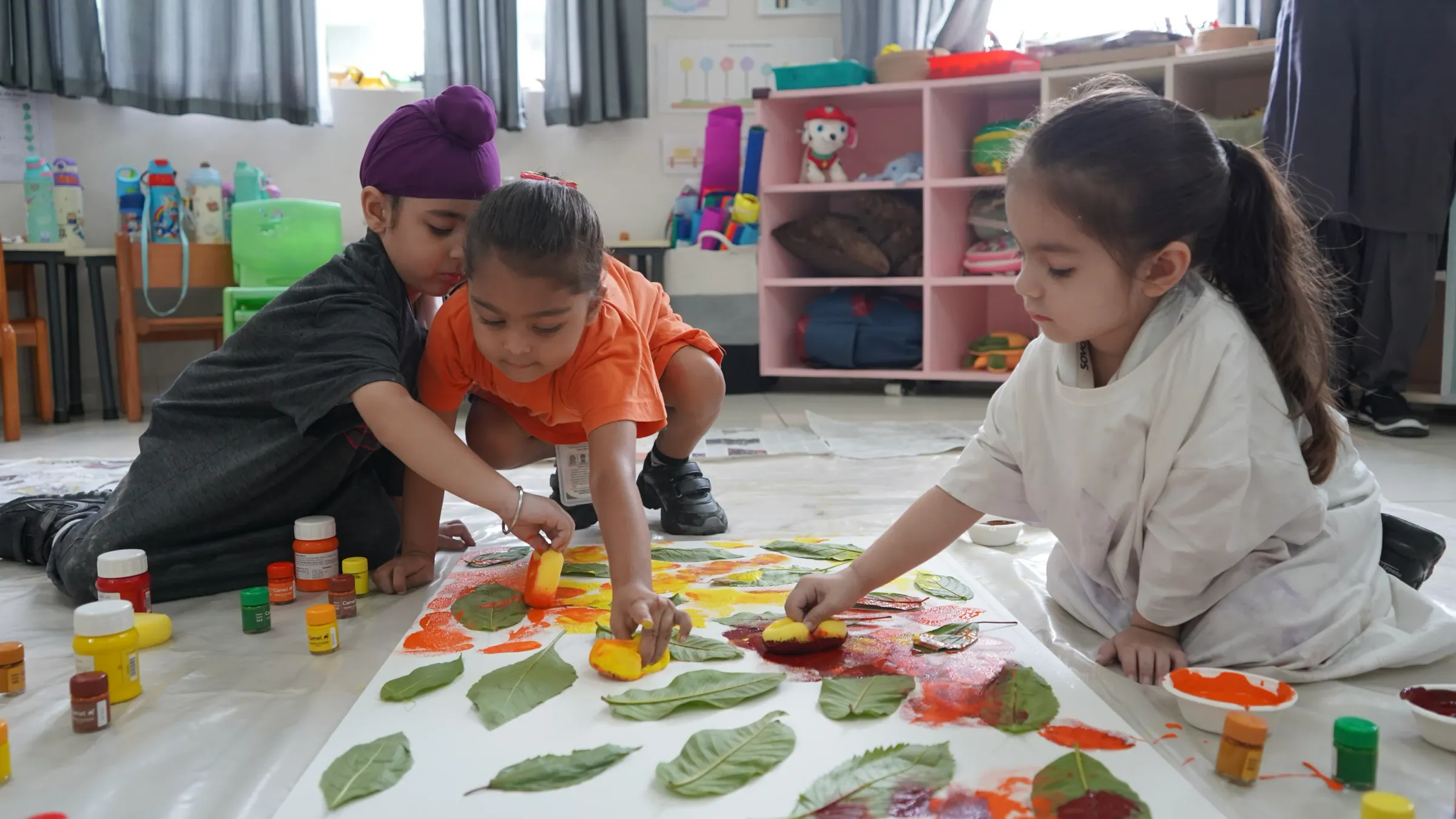 Young children printing with leaves and paint on a classroom floor