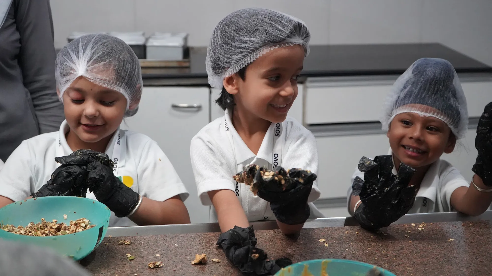 Students in hairnets and gloves making no-sugar granola bars in Monica's bakery kitchen