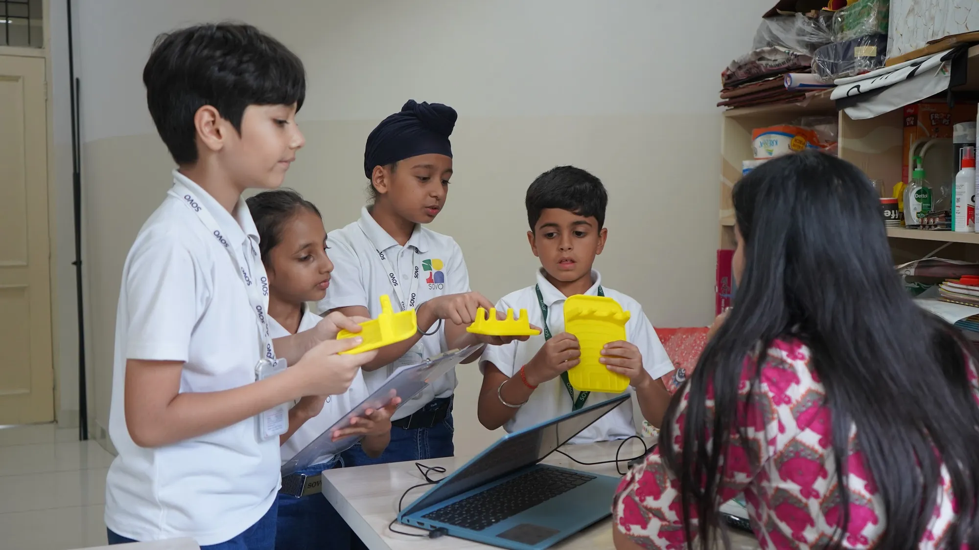 Students holding up their robotics builds with their teacher