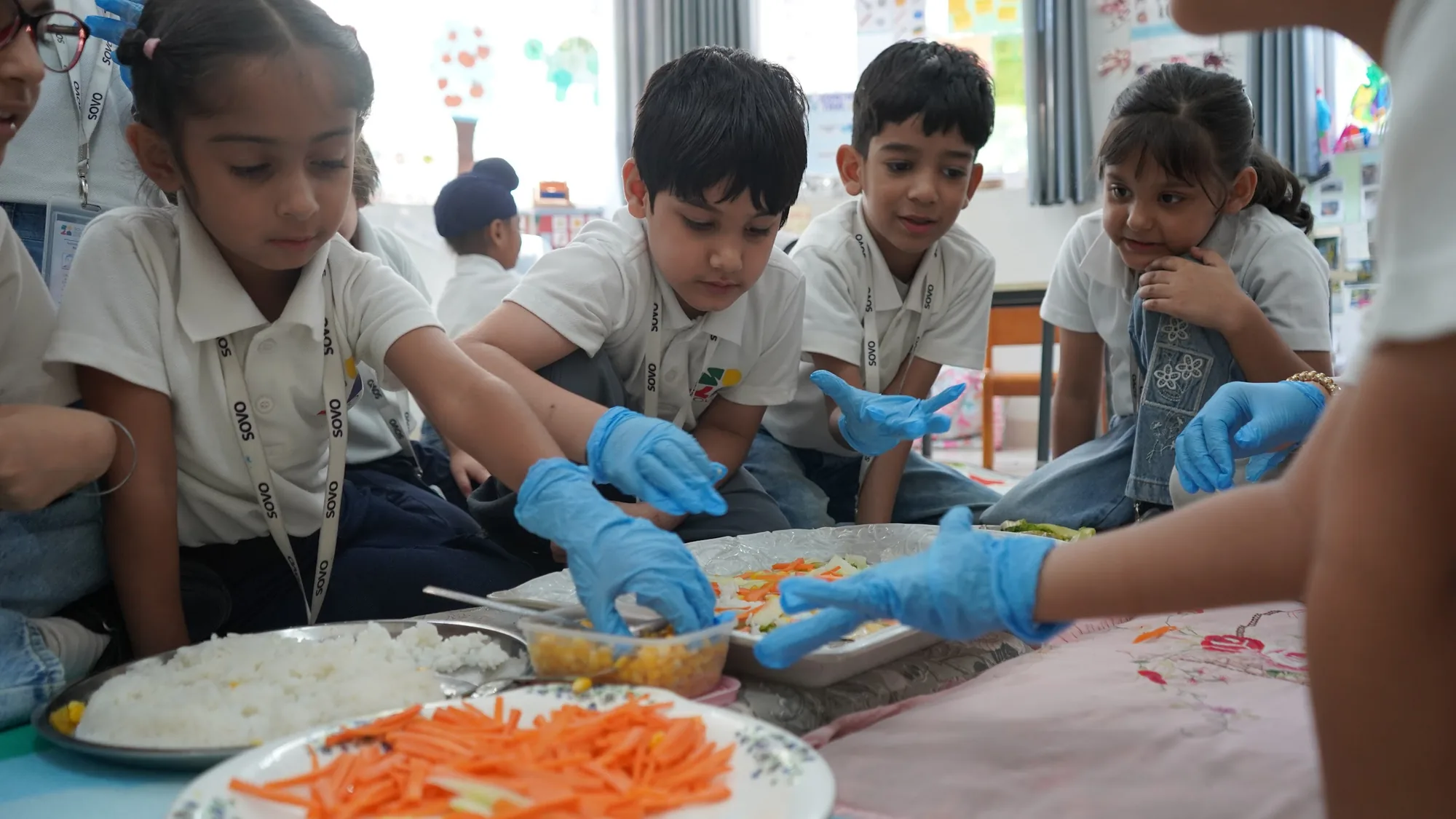 Children in blue gloves preparing a snack of rice and grated carrot together