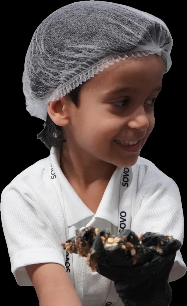 A SOVO student in a hairnet and gloves, holding granola he is making in a bakery kitchen