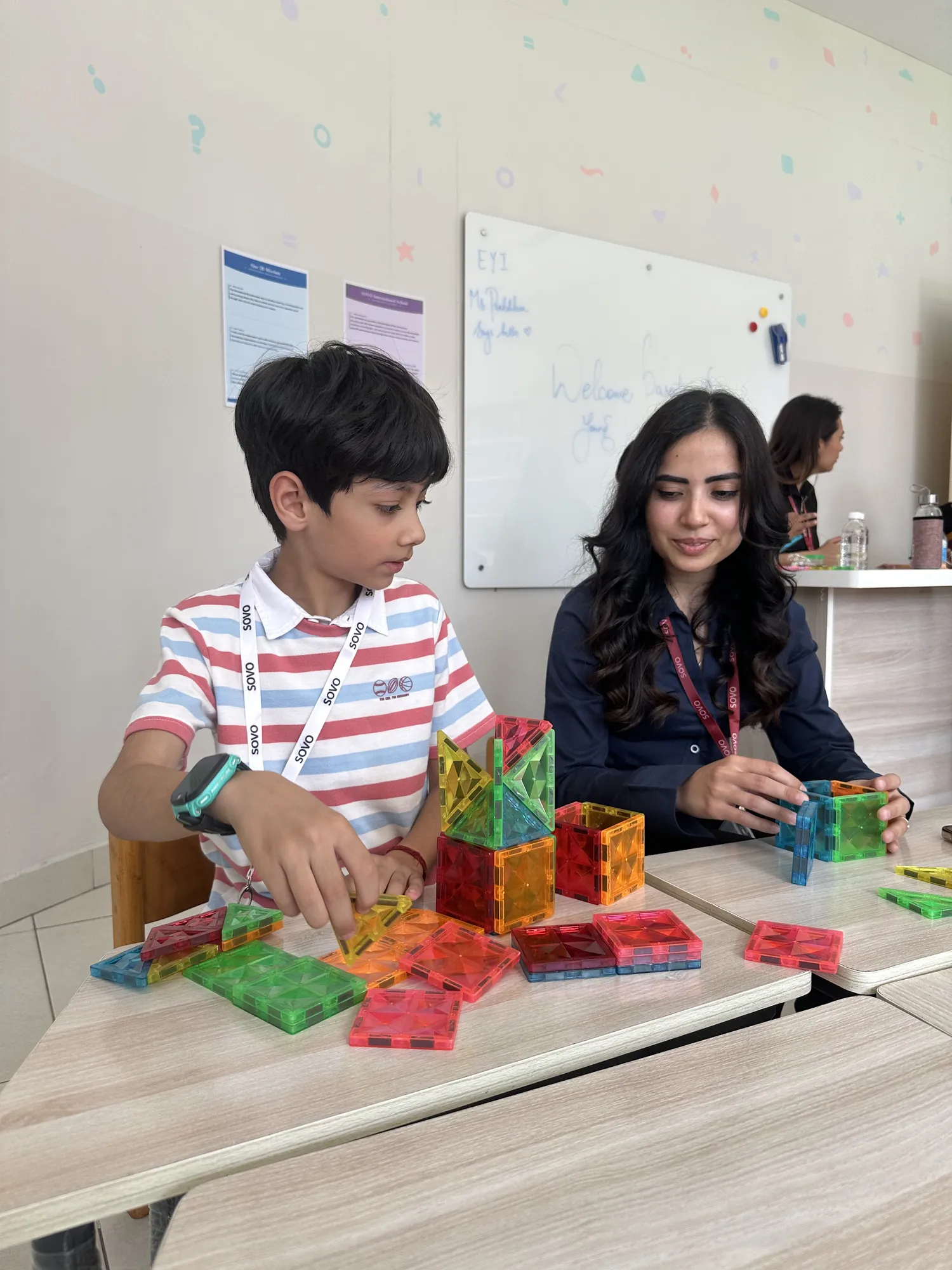 An educator building with magnetic tiles alongside a student