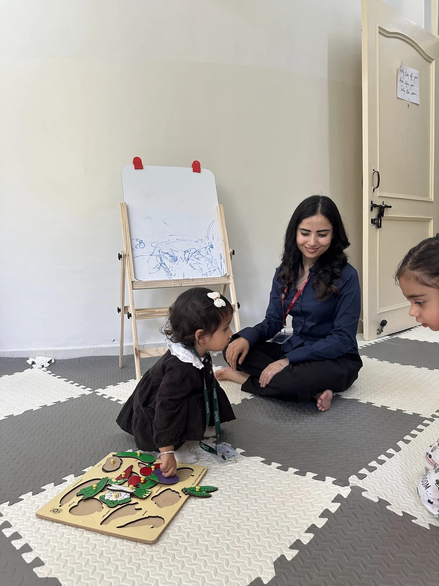 An educator sitting on the floor with a toddler doing a puzzle