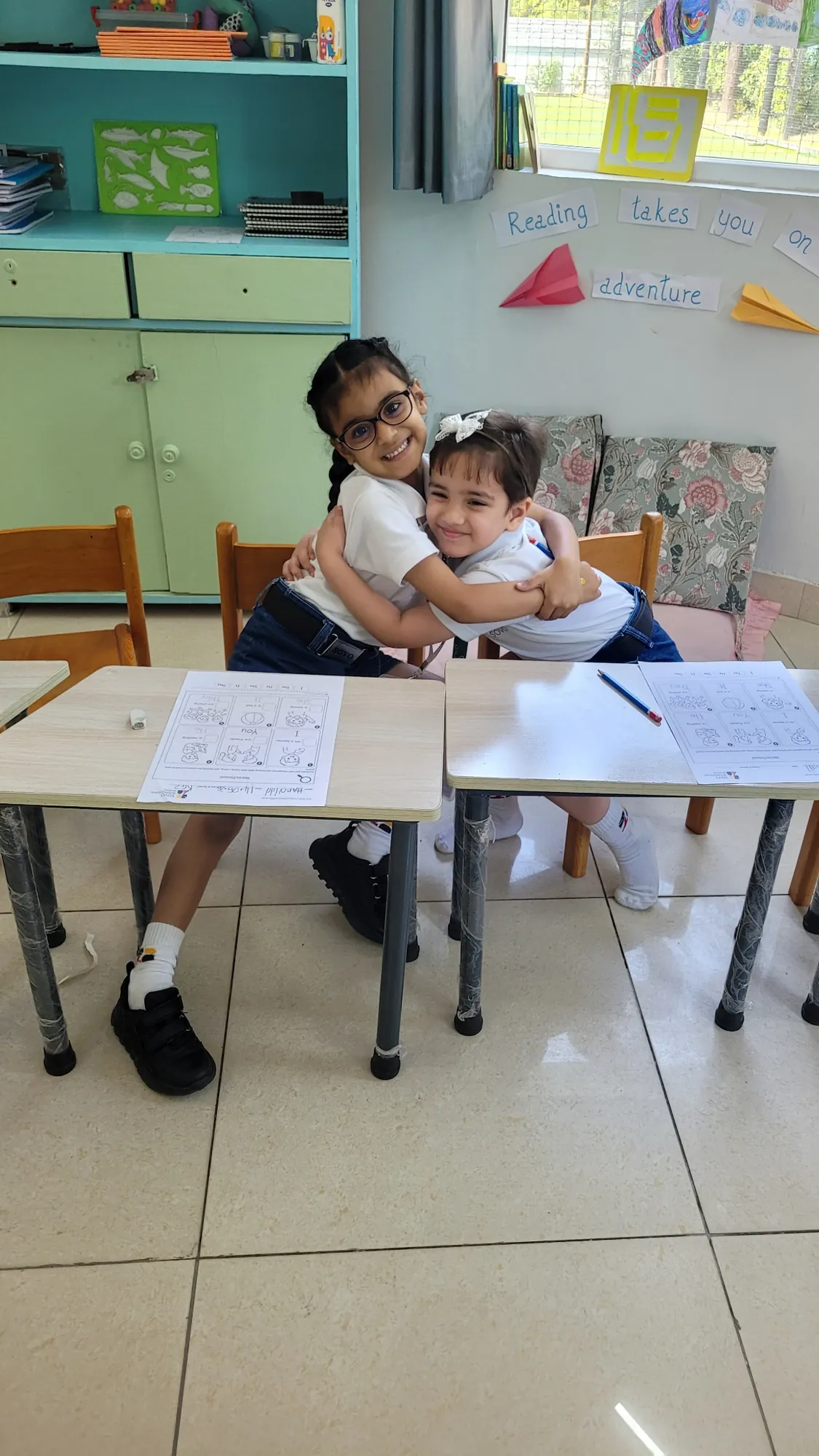 Two classmates sharing a hug at their desks